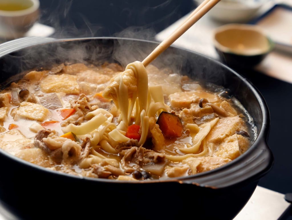写真：湯気の立ちのぼるほうとう鍋から、菜箸で麺をすくい上げる様子