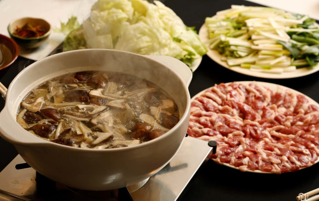 写真：きのこが煮えている鍋と、肉や野菜を盛り付けた大皿