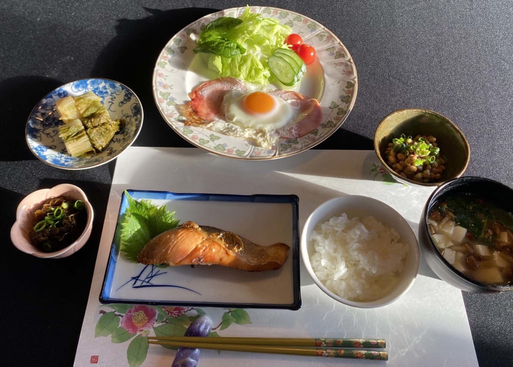 写真：左から時計回りに､もずく酢、白菜の漬け物、ハムエッグとサラダ、納豆、味噌汁、白米、焼き鮭